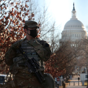 Two soldiers in camouflage uniforms with mouthguards explore the white dome of Congress in the background.