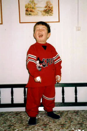 Almost three-year-old child stands on the kitchen sofa and sings in the high sky.  He's wearing a red Mickey Mouse shirt.