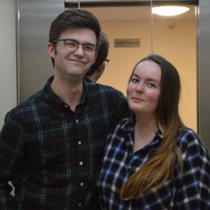 Two people stand in the elevator, smiling at the camera.