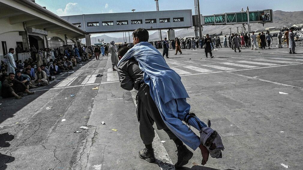 A man carries a wounded man inside the airport area in Kabul.